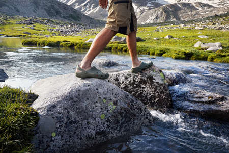 Hiking man crossing river in green shoes by stones in balance on fallen in Kazakhstanの写真素材