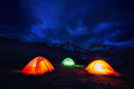 Orange yellow and green gloving tent at camping in the mountain gorge under night sky with starsの写真素材