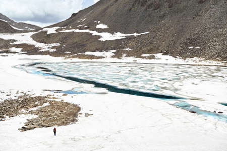 Beautiful scenery of the blue glacier mountain lake with ice pieces inside and small hiker in Kazakhstan.の写真素材