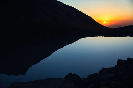 Beautiful scenery of big lake and silhouette of mountains at sunset light glow in Tien Shan Mountains, Kazakhstan.の写真素材