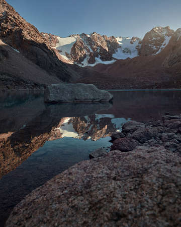 Beautiful scenery of rock at mountain lake with snow glacier at sunset in Tien Shan Mountains, Kazakhstan.の写真素材