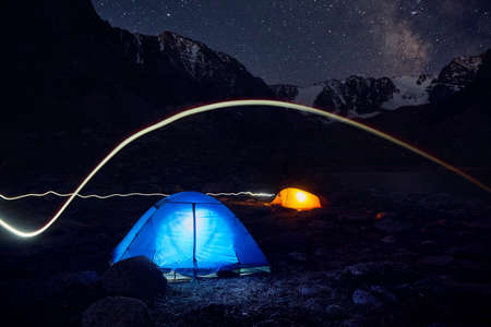 Blue and yellow gloving tent with light line at camping in the mountains under night sky with starsの写真素材