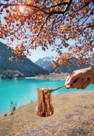 Copper Cezve for coffee in autumn lake camping in the mountains. Preparing coffee on gas stove outdoor camping conceptの写真素材