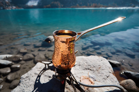 Copper Cezve for coffee in autumn lake camping in the mountains. Preparing coffee on gas stove outdoor camping conceptの写真素材
