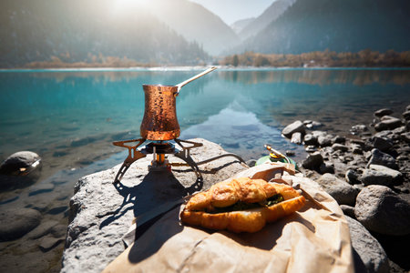 Copper Cezve with coffee on a gas stove in autumn lake camping in the mountains. Preparing coffee outdoor conceptの写真素材
