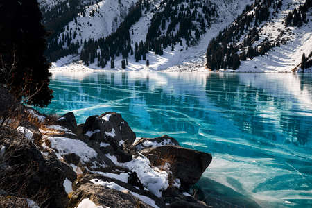 Beautiful landscape of mountain lake with blue ice and spruce forest at winter timeの写真素材