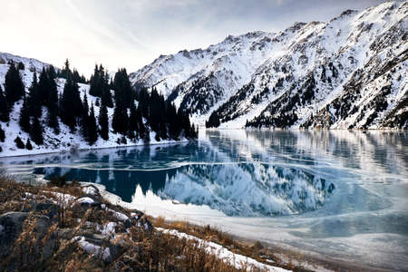 Big Almaty lake in the mountains with blue ice and spruce forest at winter time in Kazakhstanの写真素材
