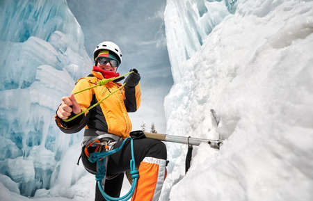 Portrait of woman climber near frozen waterfall with ice axe and rope knot in orange jacket in the mountainsの写真素材