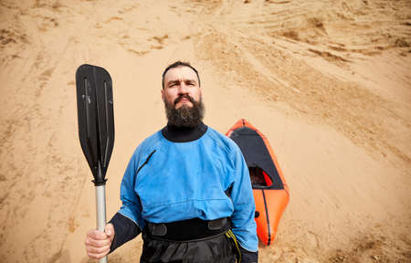 Portrait of Old man with black beard and paddle in blue jacket near orange raft sport boat at sand dune backgroundの写真素材