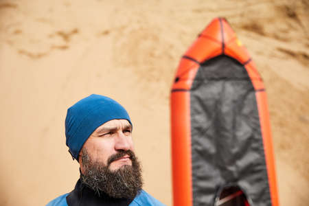 Portrait of Old man with black beard and paddle in blue jacket near orange raft sport boat at sand dune backgroundの写真素材