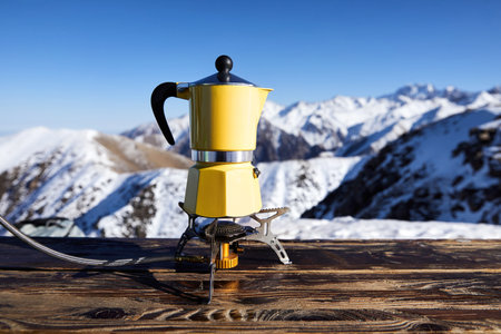Yellow moka pot coffee at snow mountain camping. Morning picnic, person cooking hot drink for breakfast in nature.の写真素材