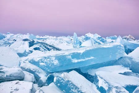 Beautiful landscape of big blue peace of Ice hummock and cracks at frozen lake with purple morning skyの写真素材