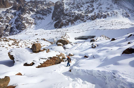 Skier man climbing with split board in high snowy mountains. Sport outdoor winter season.