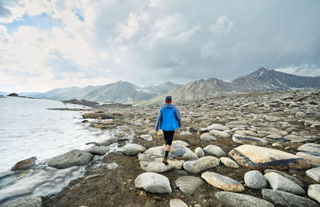 Man with in blue jacket walking on the rocky valley in the beautiful mountains against cloudy skyの写真素材
