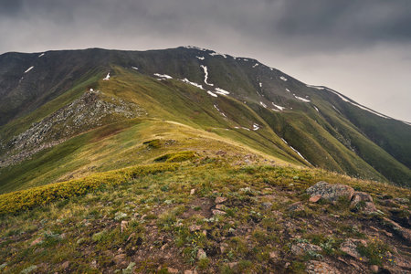 Beautiful scenery of green hills in the mountain valley and green lush meadow at dark storm sky and...