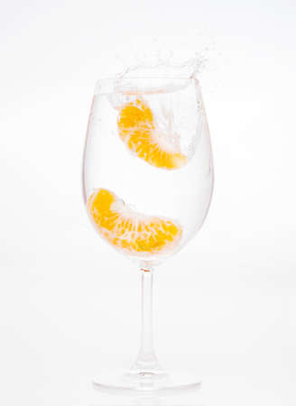 splashing orange into water glass on white backgroundの写真素材