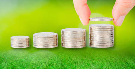 Human hand adding a golden coin in the final row of coins over blurred beautiful background. Concept...