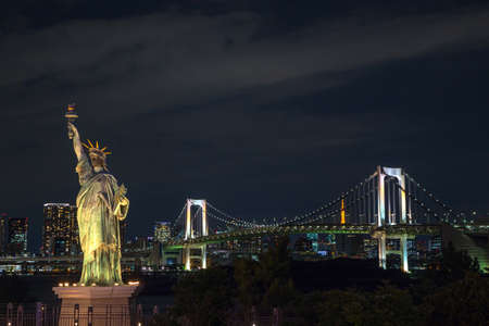 Statue of Liberty and Rainbow bridge, located at Odaiba Tokyo, with Tokyo skyline in background at nightの写真素材