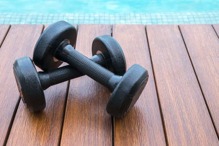 two dumbbells on wooden background near swimming poolの写真素材