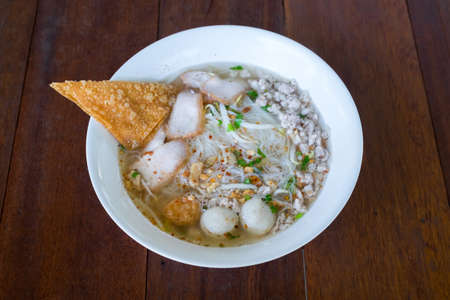 Thai Noodles Kuay Tiew  with pork and fish meat ball and vegetables with soup on wooden table