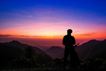 Silhouette of a young man with a bicycle at sunset sky with dramatic clouds on backgroundの写真素材