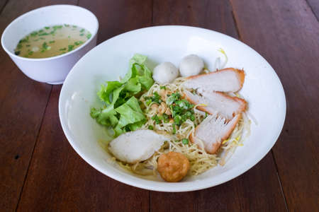 Thai Noodles Kuay Tiew  with pork and fish meat ball and vegetables with soup on wooden table