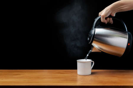 pouring water from kettle water boiler into a cup with smoke on wood table and black backgroundの写真素材