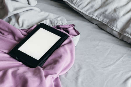 A modern black e-reader electronic book with a blank screen on a gray and purple bed. Mockup tablet on microfiber beddingの写真素材