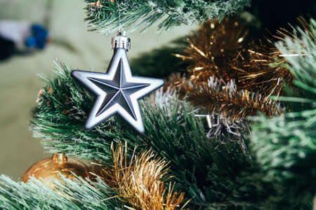 Silver star hanging on a branch of an artificial Christmas tree decorated with a gold garlandの写真素材