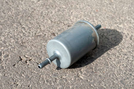 Used fuel filter on a gray asphalt on a sunny day. Filter element in the fuel line that traps...