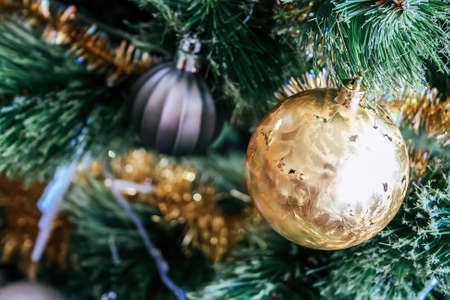 A golden ball hangs on an artificial Christmas tree decorated with a gold garlandの写真素材