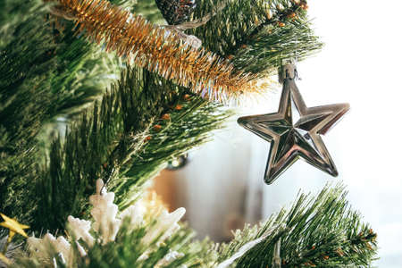 Silver star hanging on a branch of an artificial Christmas treeの写真素材