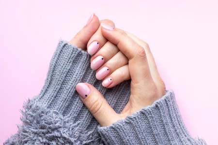 Female hands in a gray fluffy knitted sweater with trendy beautiful manicure - pink nude nails with black small dots on a pink backgroundの写真素材