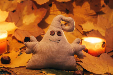 A toy monster with button eyes sits among leaves and candlesの写真素材