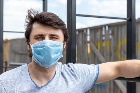 Street portrait of a white caucasian man in protective blue medical mask in a period of pandemic coronavirus covid-19. Male in a disposable respirator to protect against infection with virus outdoorsの写真素材