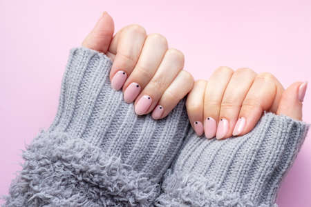 Female hands in a gray fluffy knitted sweater with trendy beautiful manicure - pink nude nails with black small dots on a pink backgroundの写真素材