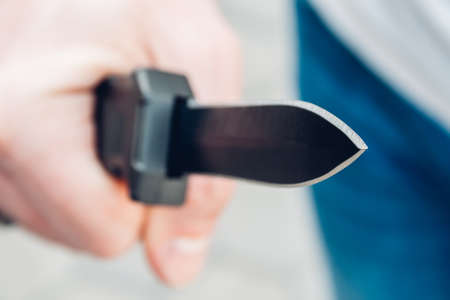 Closeup view of a man's hand with a black pocket folding knife blade facing forward. Selective focusの写真素材