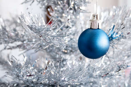 Closeup view of a blue matte ball hanging on a silver artificial Christmas tree for a family holiday. Selective focusの写真素材