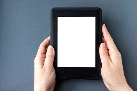 A modern black electronic book with a white blank empty screen in female hands on a gray paper background. Mockup tablet closeupの写真素材