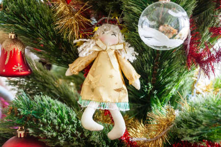 Green artificial Christmas tree decorated with angel toy with stars, transparent ball, red bell and red and golden garlands. Home decoration for a family holiday. Selective focusの写真素材