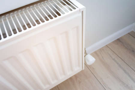 Closeup view of a home heating radiator in a living room with wooden floor and light wall. Creating and keeping a comfortable temperature in the house in the winter. Visual heat radiationの写真素材
