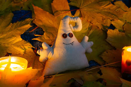 A toy monster with button eyes sits among leaves and candlesの写真素材