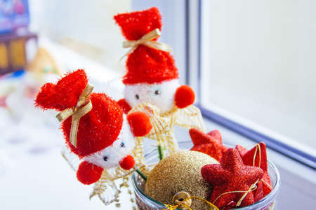 A vase stands at the window filled with red and yellow Christmas tree toys. Two snowmen on sticks are on top.の写真素材