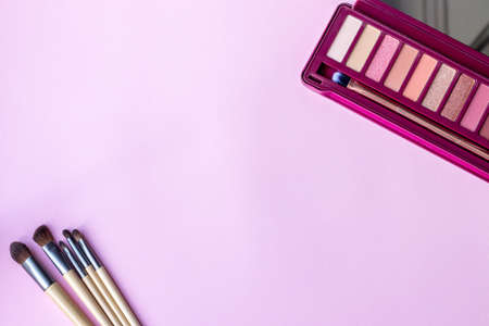 Colorful eye shadow palette in pink colors and a set of makeup brushes on a pink, lilac paper background with copy space. Professional color palette for eye makeup with matte and shimmer shadowsの写真素材