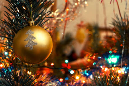 Golden ball with silver painted tree hanging on a Christmas tree among the lightsの写真素材
