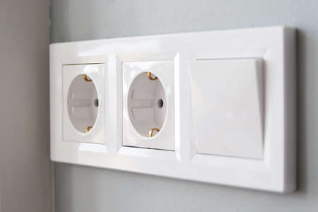A closeup diagonal view of a group of white european electrical outlets and a switch located on a painted gray wallの写真素材