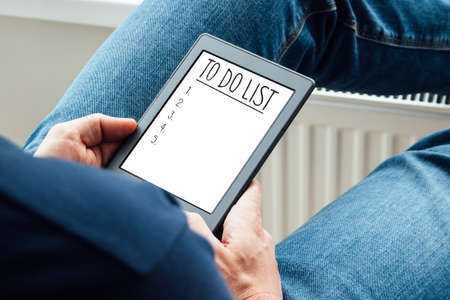 To do list in modern gray tablet in man hands. Planning when quarantine ends at home by the windowの写真素材