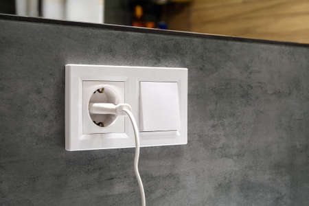 A closeup diagonal view of a group of white european electrical outlet with a plug inserted into it...