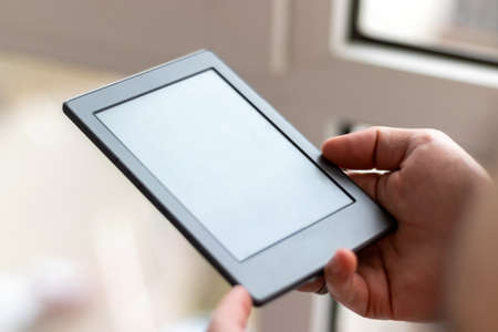 Male hands with modern e-book with blank screen closeup. Reading at home on the balcony with a pocket readerの写真素材