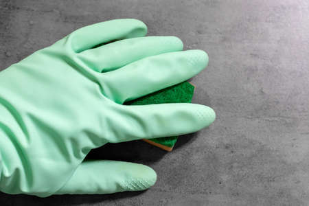 A hand in a mint green rubber glove wipes wet gray tile concrete wall with an orange sponge. Cleaning in a modern bathroom. Selective focusの写真素材